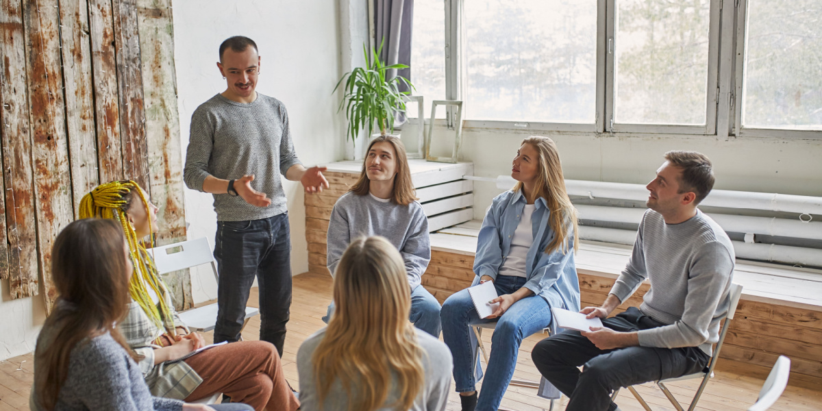 Group of six people sitting in a circle, some taking notes.