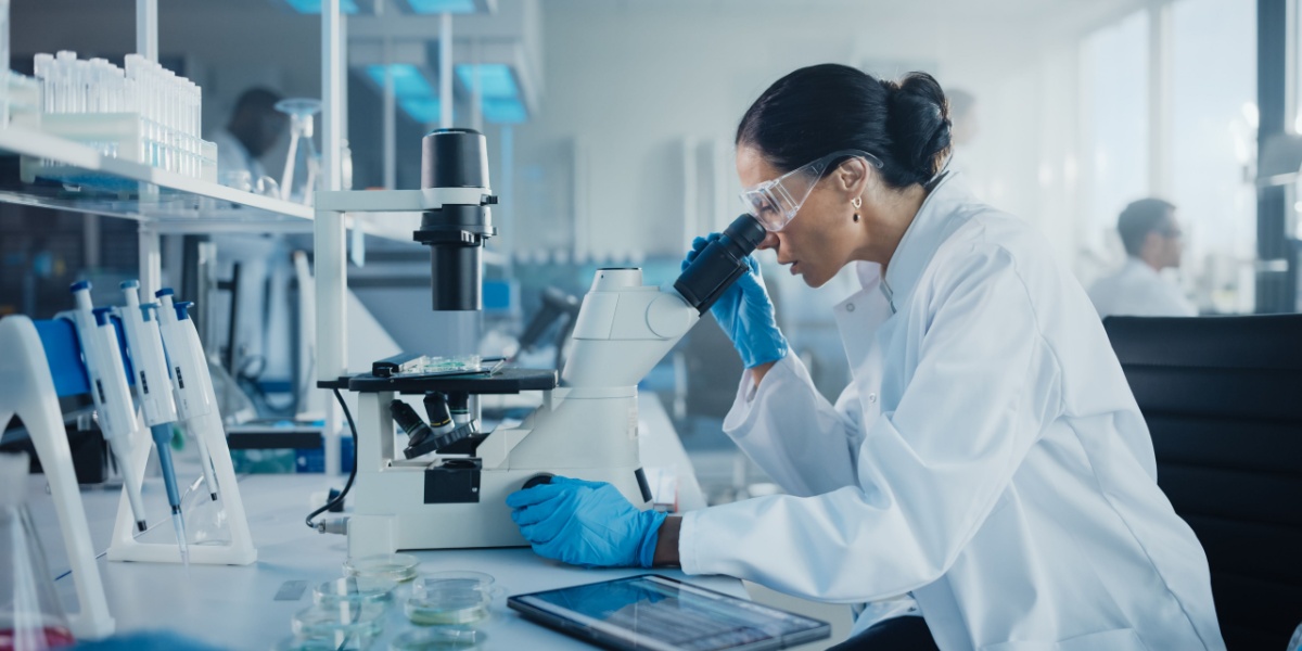 Scientist in lab coat using a microscope, surrounded by lab equipment.
