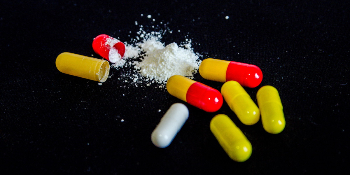 Red, yellow, and white capsules with powder on dark surface.
