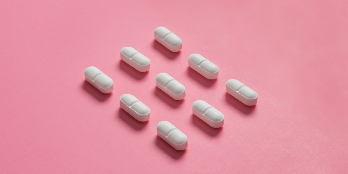 Nine white capsules arranged diagonally on a pink background.