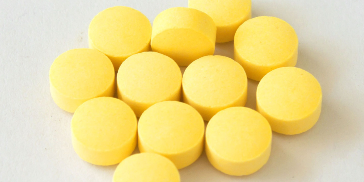 Eleven yellow round pills arranged on a white surface.