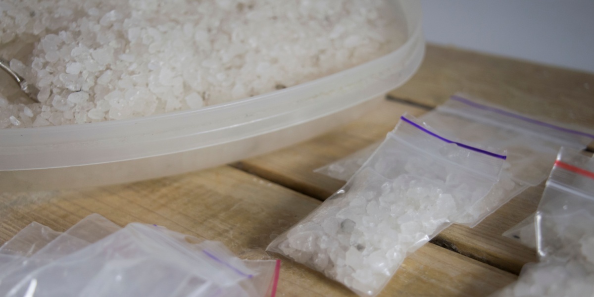 Close-up of white crystals in plastic container and ziplock bags on a wooden surface.