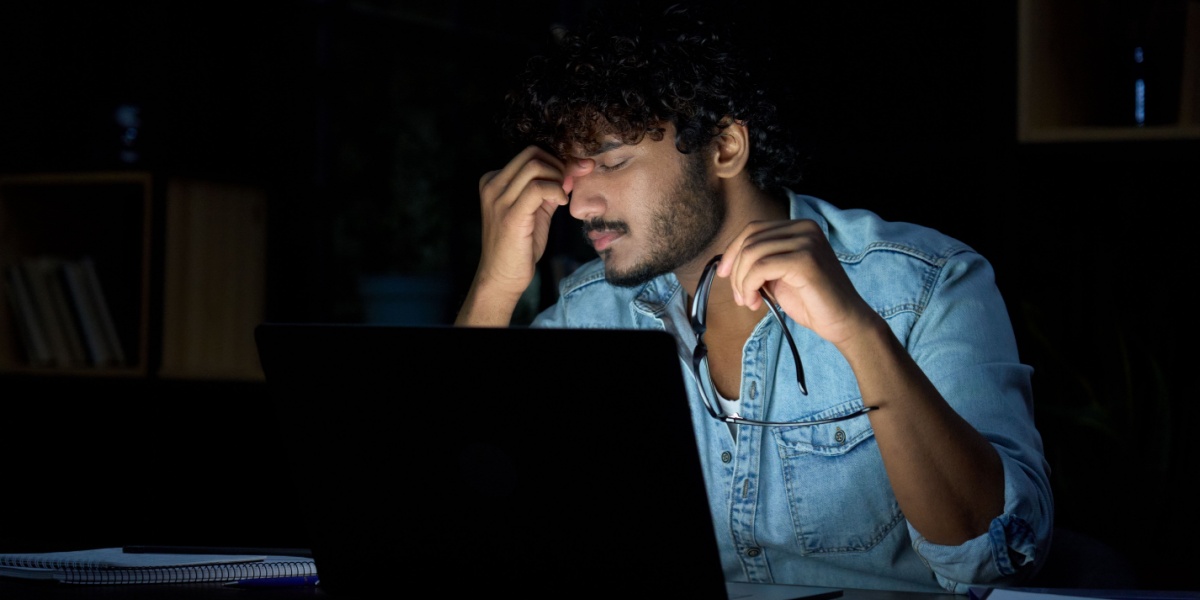 Person in a denim shirt sitting at a desk with a laptop.