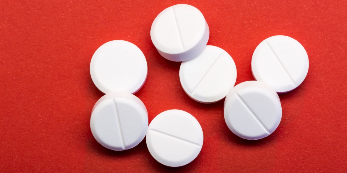 Eight white round tablets with score marks on a red surface.
