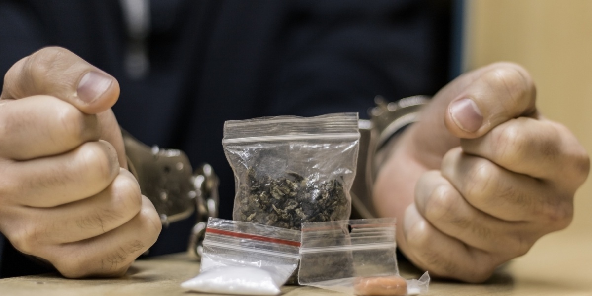 Handcuffed hands with small bags containing various substances on a table.