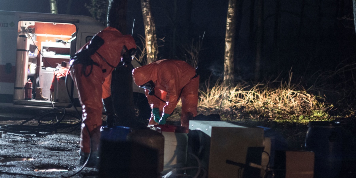 Two people in orange hazmat suits working beside an open van at night.