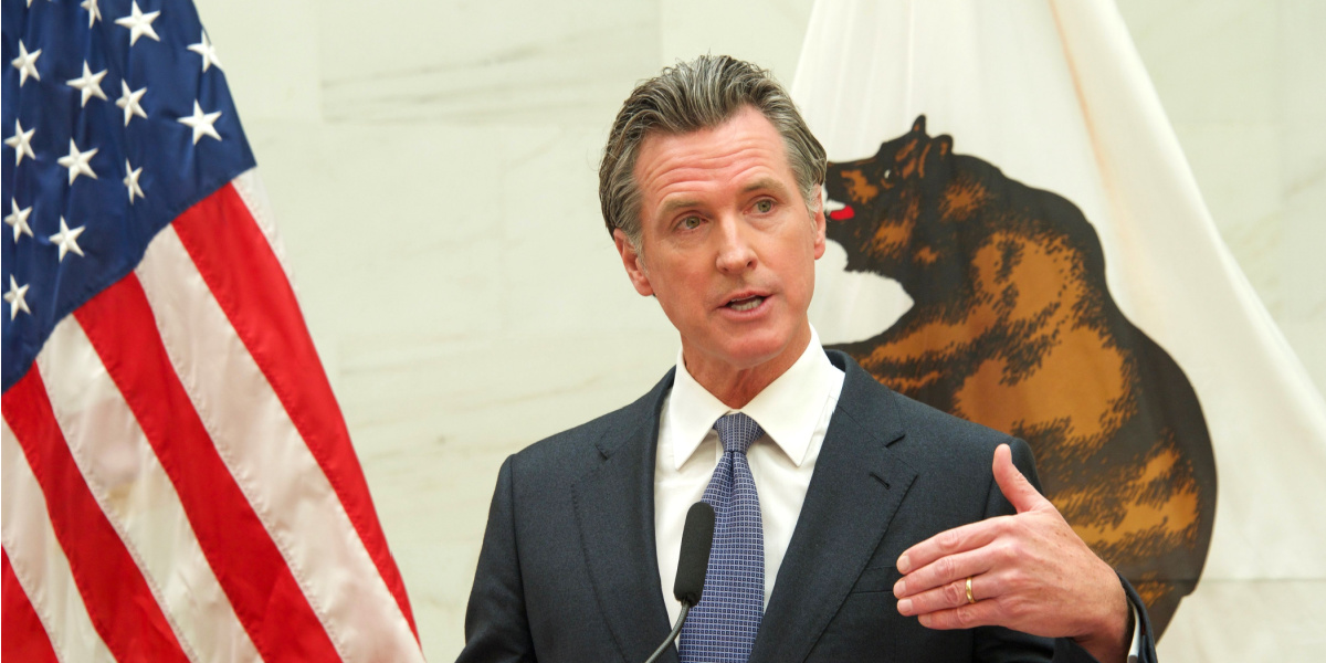 A person in a suit speaking with American and California flags behind.