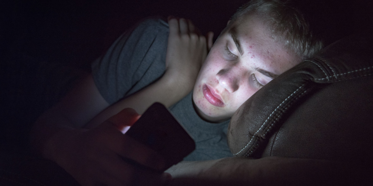 A person lies in the dark, illuminated by a smartphone.