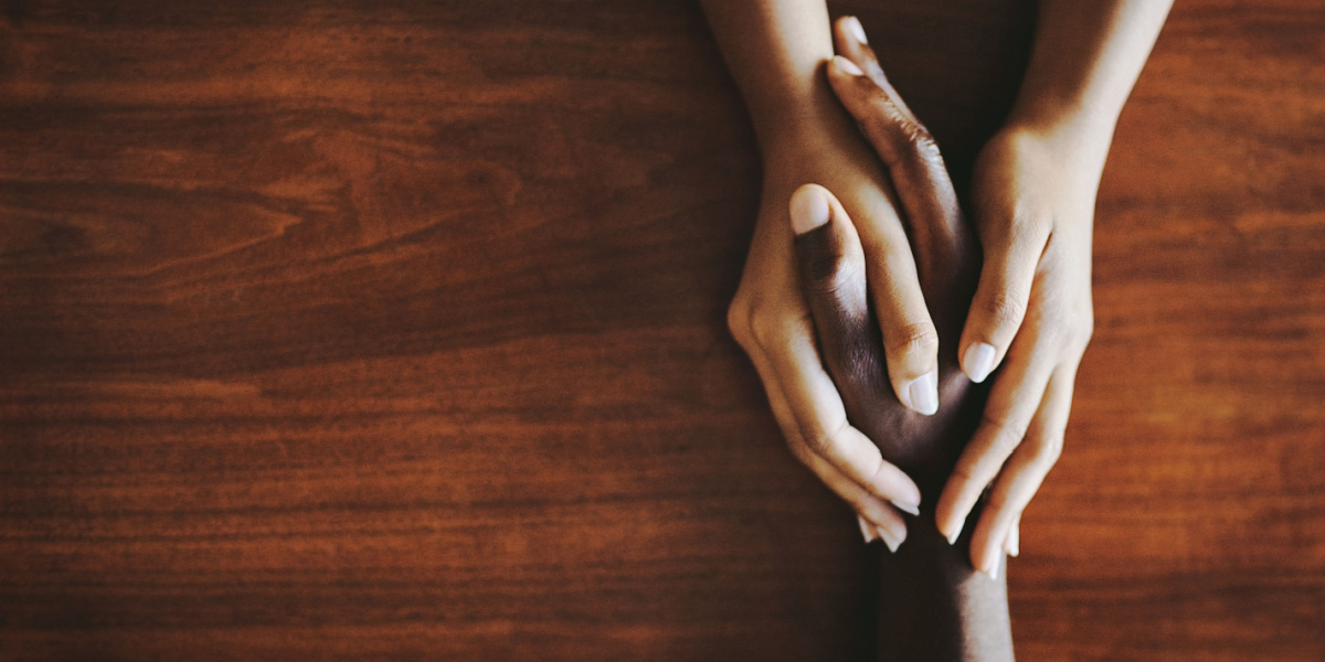 Two hands, one dark-skinned and one light-skinned, clasped over a wooden surface.