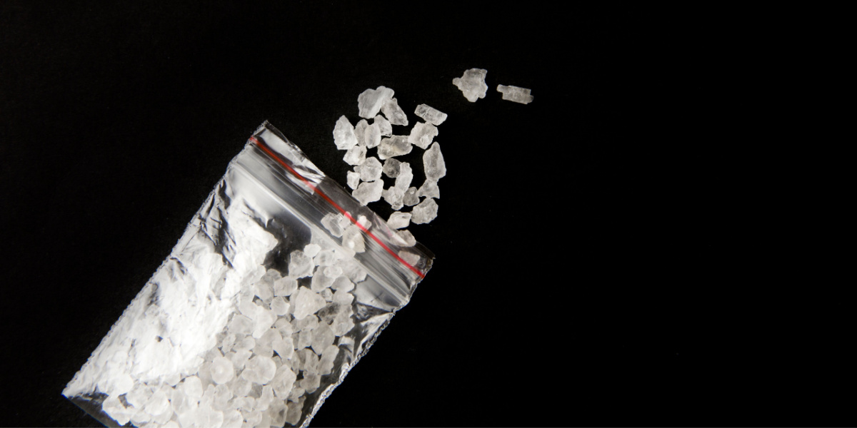 Small plastic bag spilling white crystalline substance onto black background.