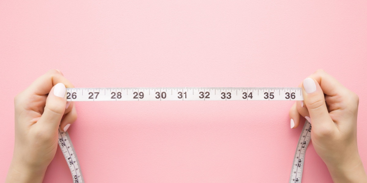 Hands holding a measuring tape against a pink background.