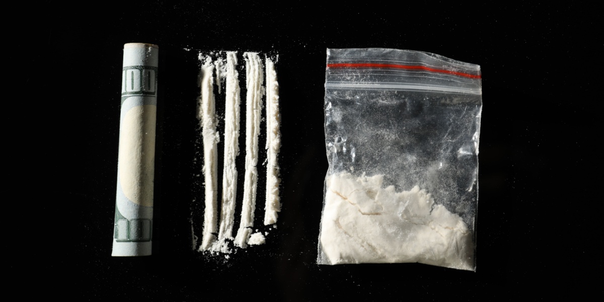 rolled up 100 dollar bill, four lines of cocaine, cocaine in clear bag on black background