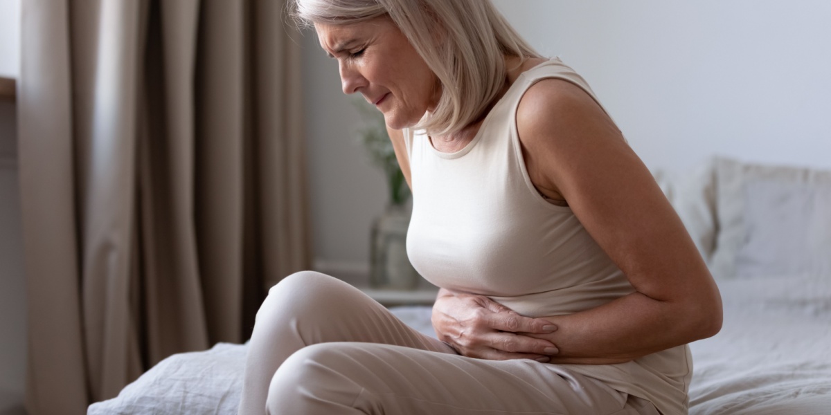 a woman in cream tank top with a stomach ache from kratom withdrawal