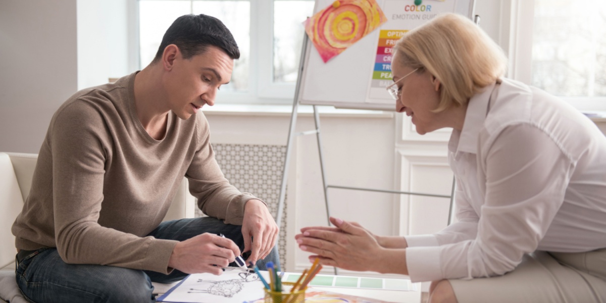 a photo of a man in an art therapy session with a therapist across him