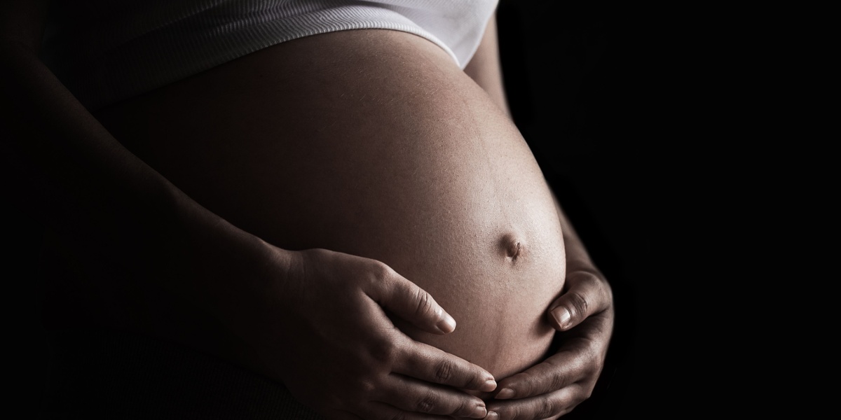 a close up photo of a woman holding her naked pregnant belly with dark lighting and a black background