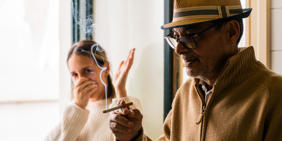 a photo of a man holding a cigarette with a woman pinching her nose trying to avoid inhaling secondhand smoke