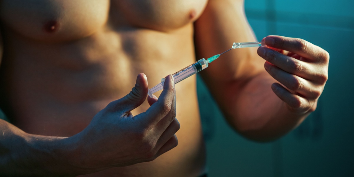 a close up photo of a mascular man holding an injection needle with anabolic steroids