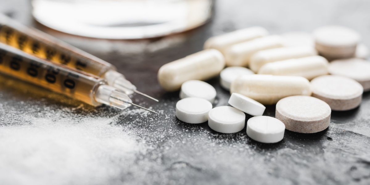 a close up photo of a syringe with stimulants and opioid pills for speedballing