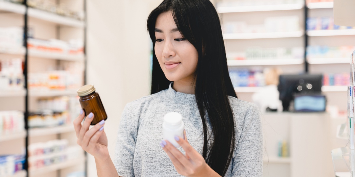an Asian woman holding up a Concerta pill bottle on one hand and a Vyvanse pill bottle on the other
