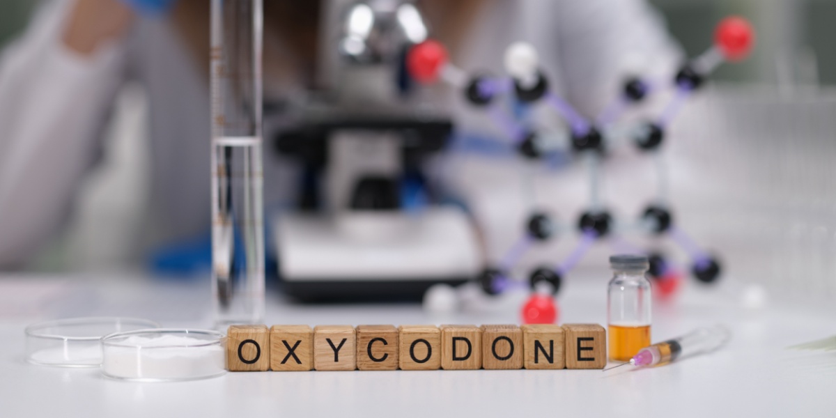 a blurry photo of a lab and a scientist in a lab gown with tile blocks in front spelling out Oxycodone