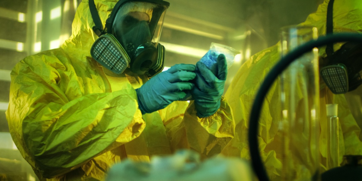 a half-body photo of a person in a hazmat suit holding a pack of meth while in a meth lab