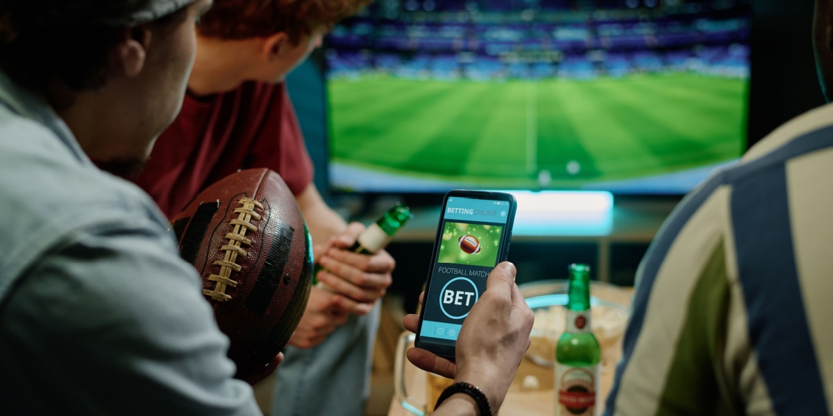 a photo of a group of male friends watching a game and one of the men holding his smartphone to place a bet