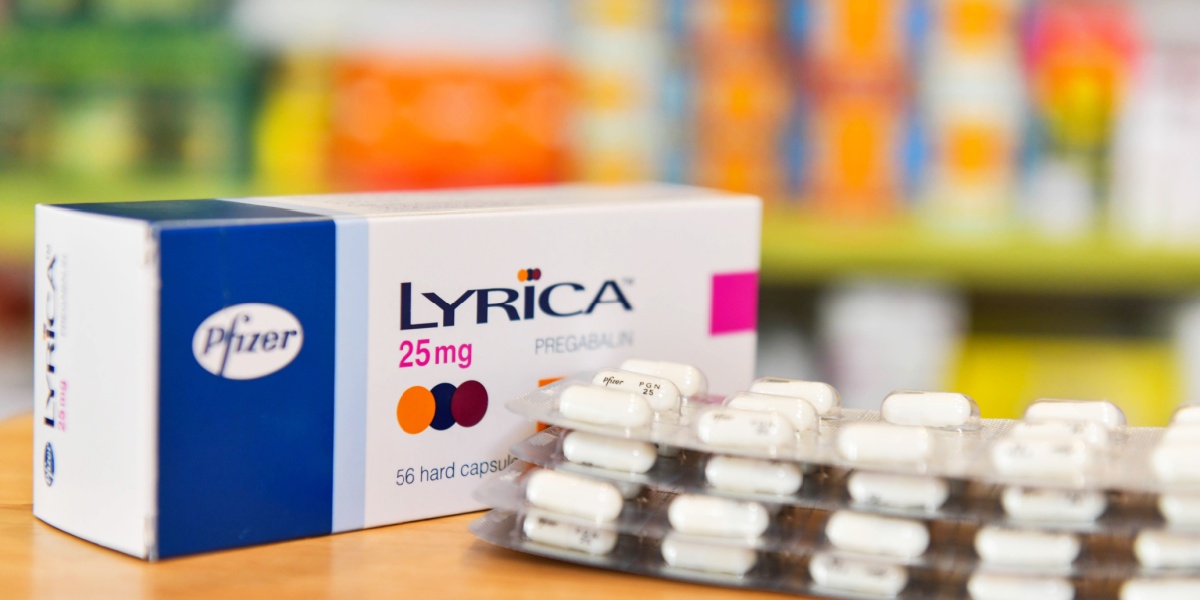 a close up photo of a Lyrica (pregabalin) box and blister packs, with different kinds of medications and substances blurred in the background