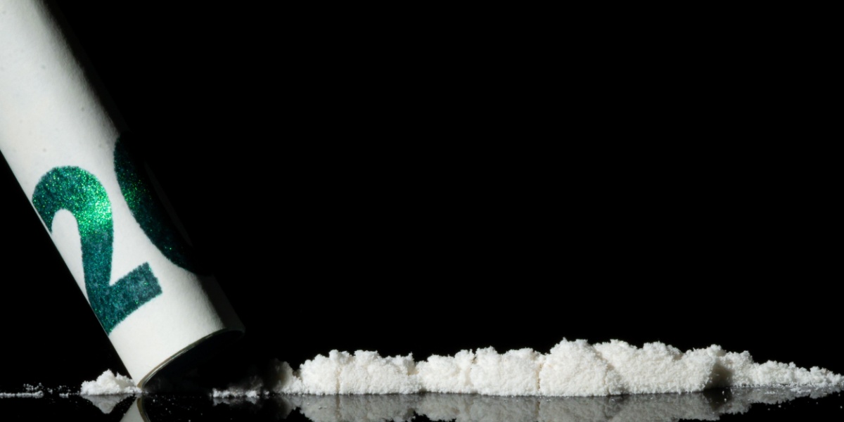 a close up photo of a rolled up dollar bill and mephedrone against a black background