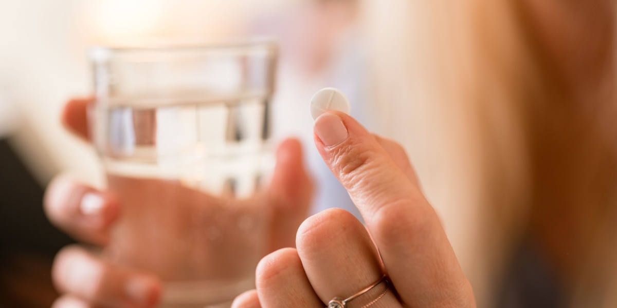 a close up of a hand holding a Lunesta pill on one hand and a glass of water on the other