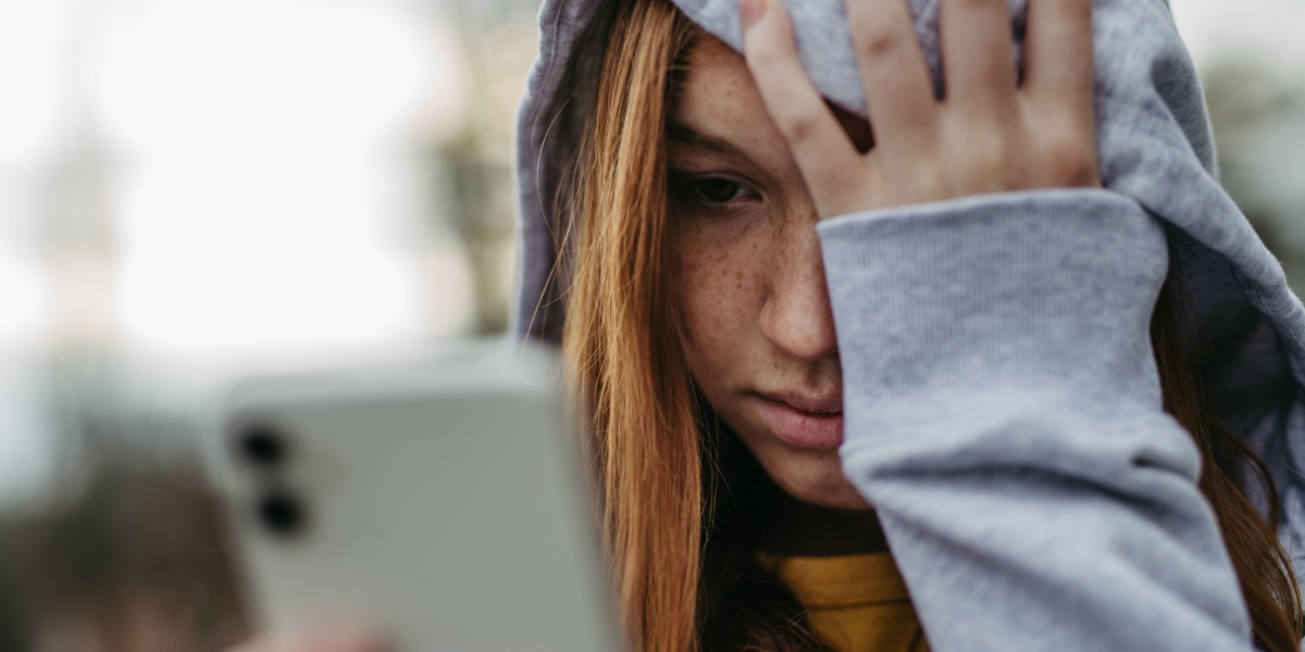 a close up photo of a young teenager in a hoodie looking distressed after being cyberbullied
