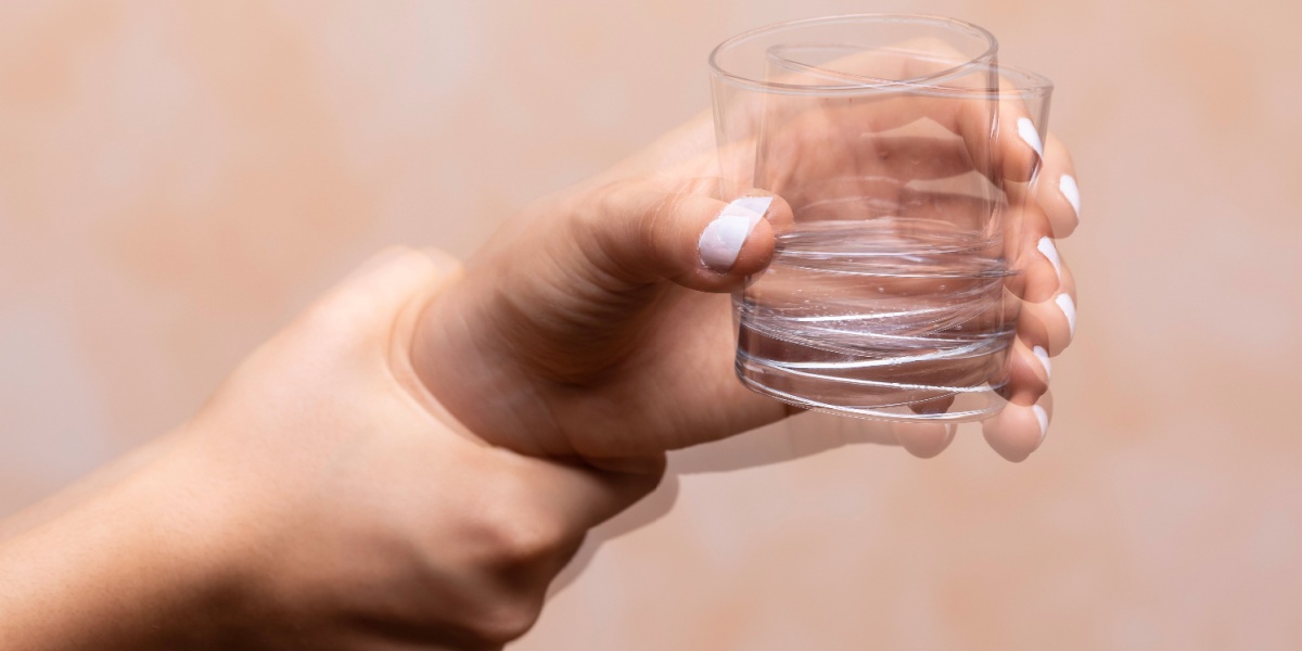 a close up of a shaking hand holding a glass of alcohol because of delirium tremens