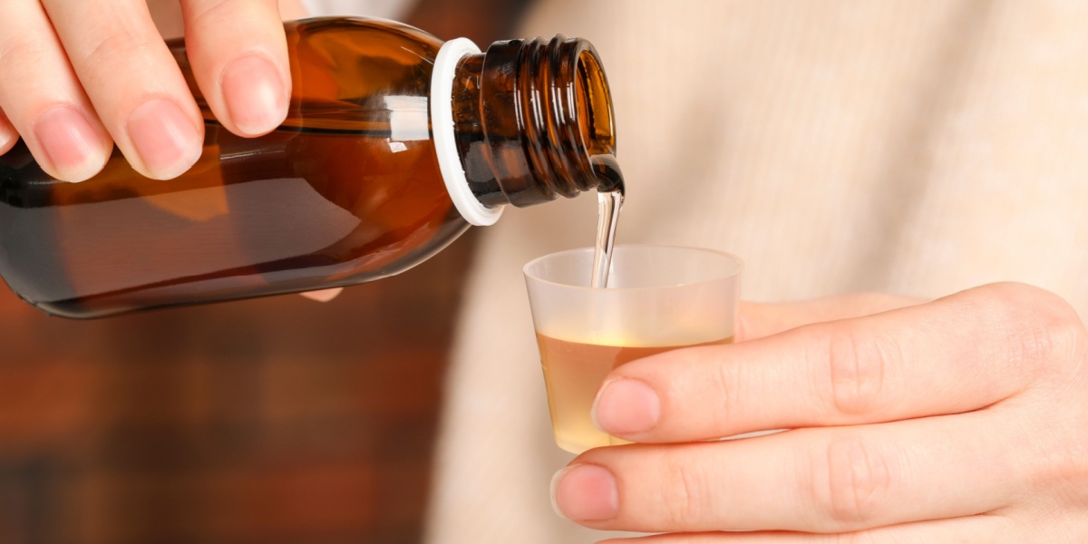 a close up of a pair of hands pouring DXM into a measuring cup for the right dosage