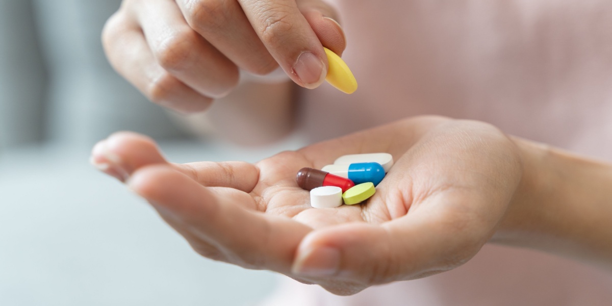 a close up photo of a woman's hand with a handful of different pills, the other hand carried a Baclofen pill