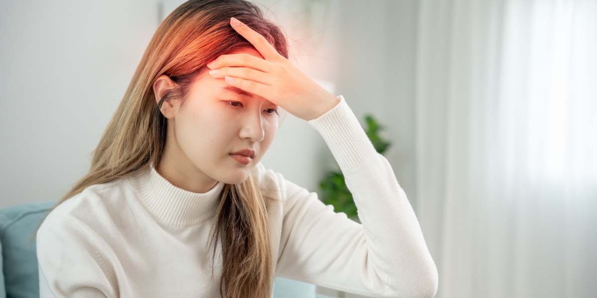 a close up photo of an Asian woman massaging her head due to headaches caused by Baclofen side effects