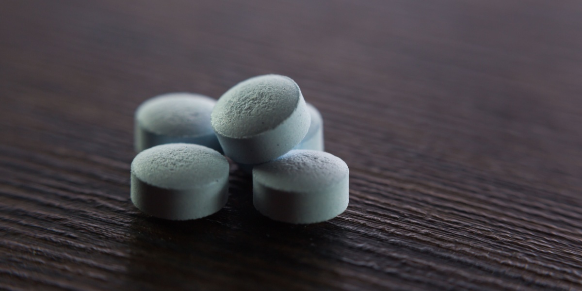 a close up photo of a clumped up blues (drug) pills on top of a dark wooden table