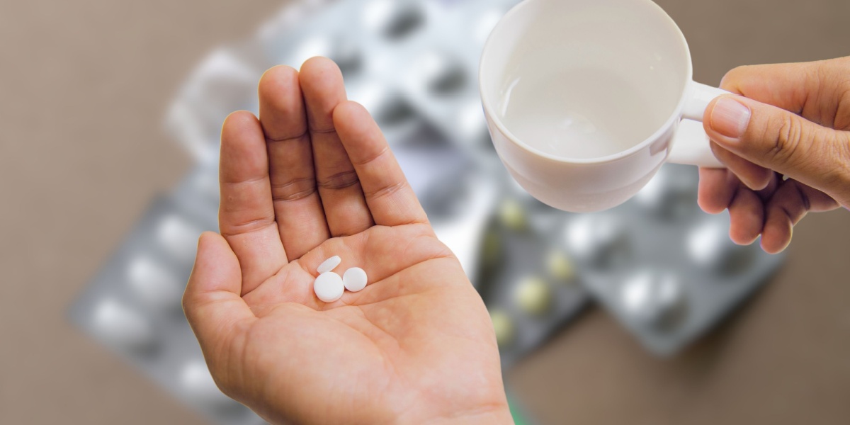a bird's eye view photo of a pair of hands holding Lexapro pills and a cup of water, with other drugs and substances on the background