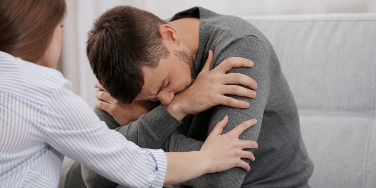 a photo of a young man hunched over and looking miserable, suffering from dry drunk syndrome while a woman tries to offer support