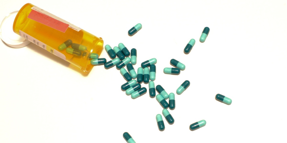 a photo of a toppled over orange pill bottle with hydroxyzine pills spilling over a white background