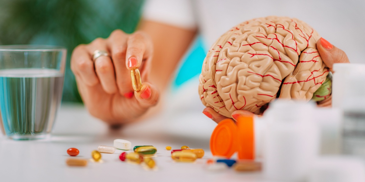 a photo of a hand holding a brain model and a bunch of supplements and drugs like nootropics spilled over the table