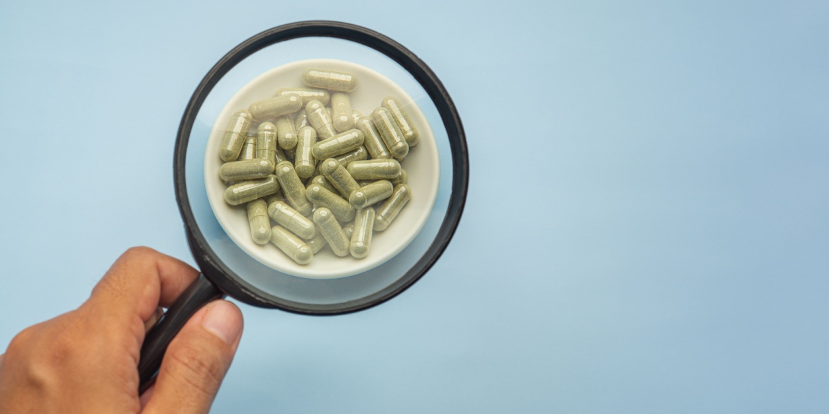close-up photo of a hand holding a magnifying glass over a saucer full of capsules with 7-OH or 7-hydroxymitragynine