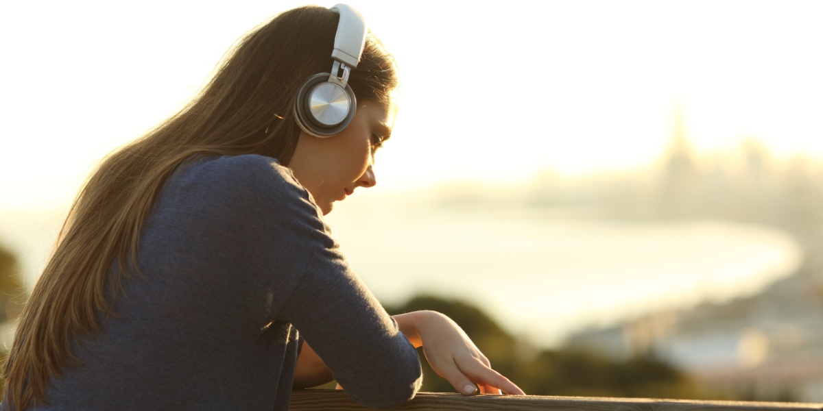 a close up photo of a Caucasian girl with brunette hair with headphones over her head and looking out into a view