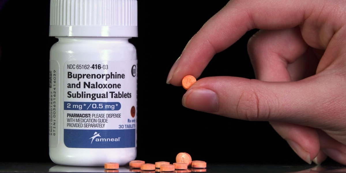 a close up photo of a buprenorphine tablet held between fingers and a buprenorphine pill bottle beside it