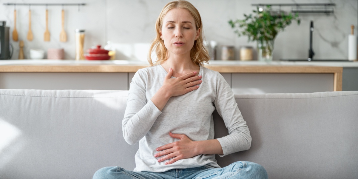 a Caucasian woman sitting on her sofa and trying to practice breathing exercises to manage her anxiety