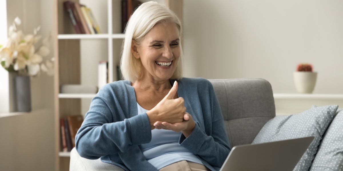 an elderly Caucasian woman smiling and holding a thumb up while in a meeting session from In The Rooms