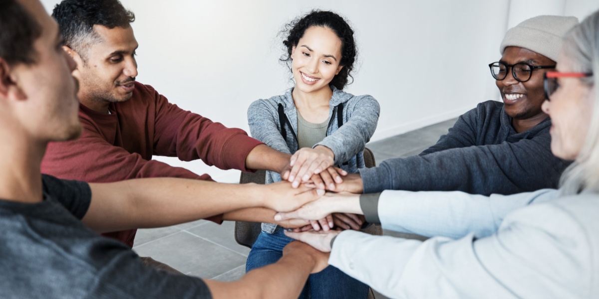 A photo of a diverse group of people joining their hands together to celebrate a support group session for alcohol recovery