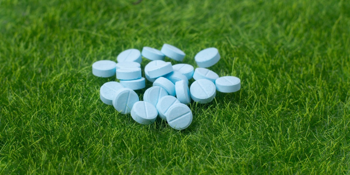 a close up photo of a clump of blue, circle dexmethylphenidate pills on the grass