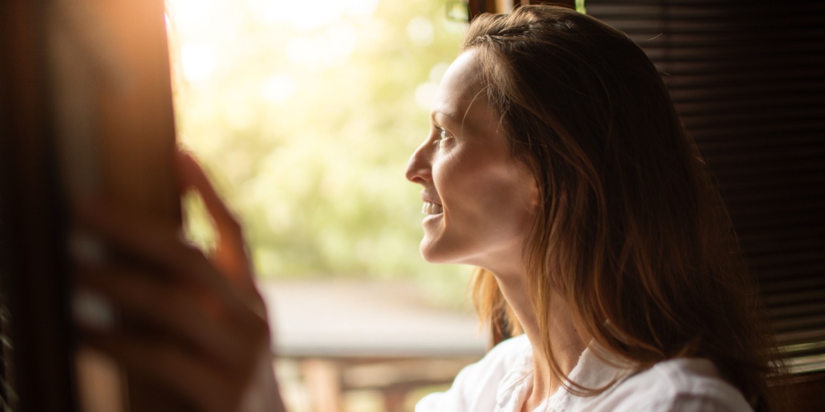 a close up photo of a woman opening a window and feeling good after quitting alcohol