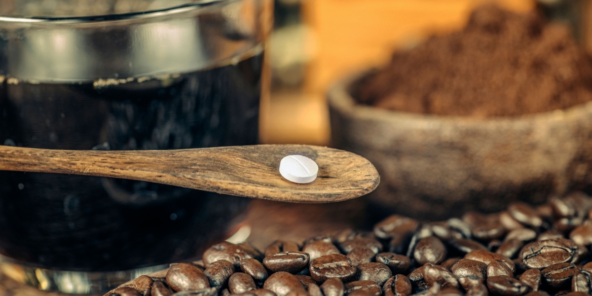 a close up photo of a caffeine pill surrounded by espresso, ground coffee, and coffee beans on the background