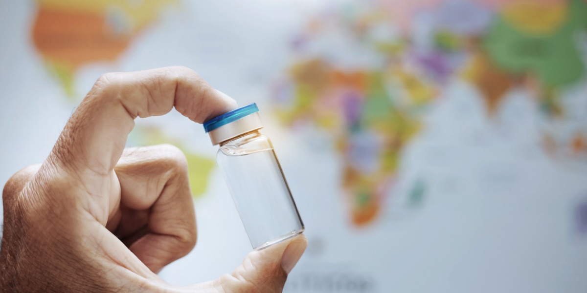 A close up photo of a hand holding a small vial of fentanyl and a map of the world blurred in the background