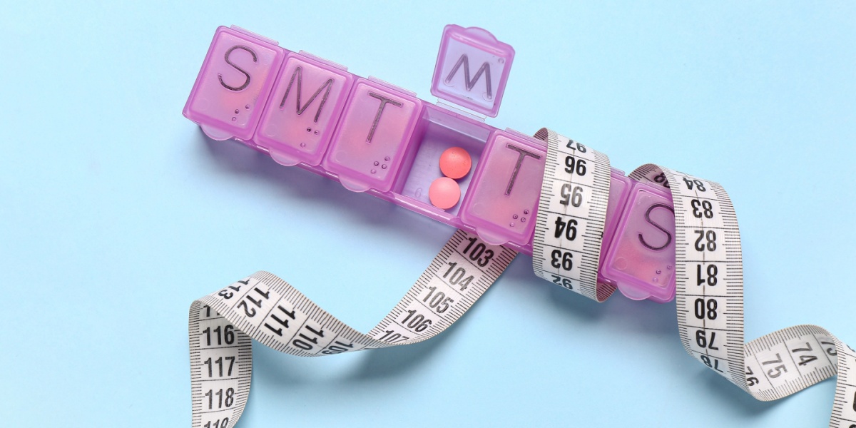 A close up photo of Vilazodone tablets inside a pill box with a measuring tape wrapped around the pill box